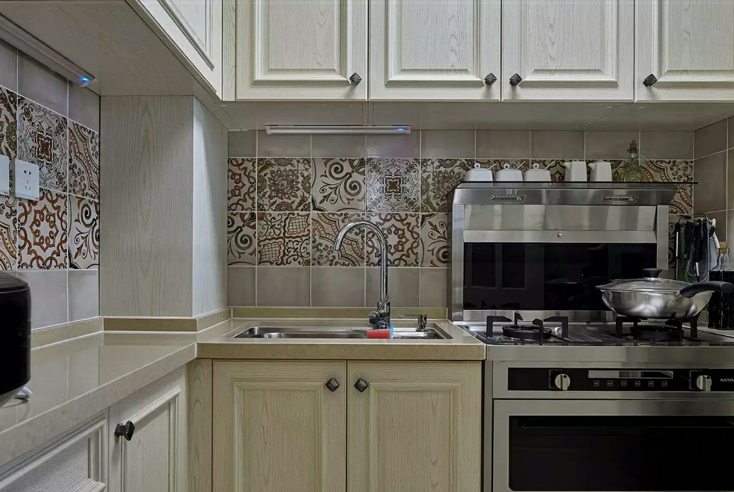 厨房中用米黄色的台面和浅木色的柜板强调空间的干净明亮，但难免有点单调。为了色彩上显得更加开胃，设计加入了美式古典的彩砖，将自然与浪漫融入空间