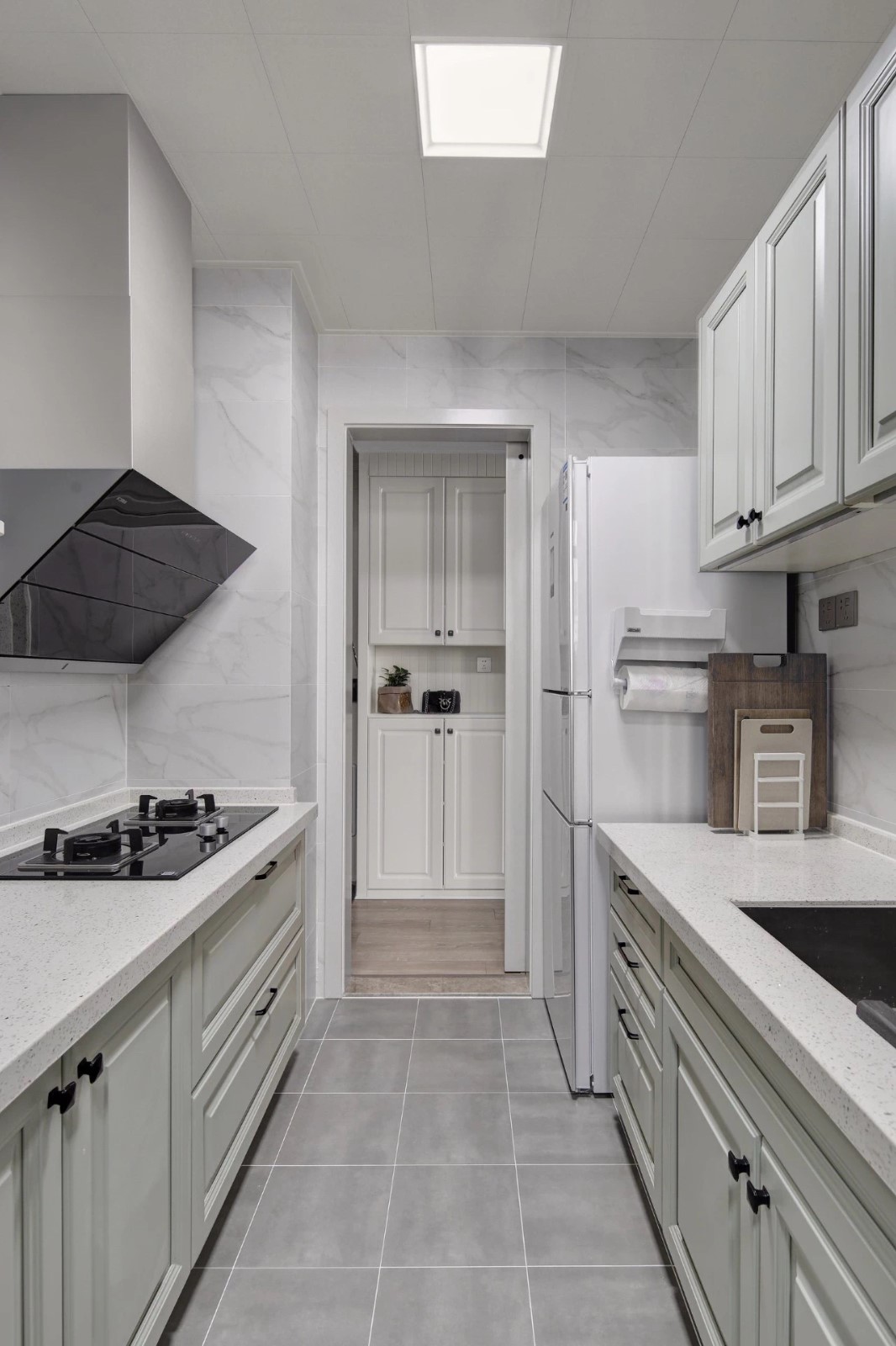 厨房地面铺设灰色哑光砖,墙面铺设大理石纹瓷砖,搭配上灰白色的橱柜